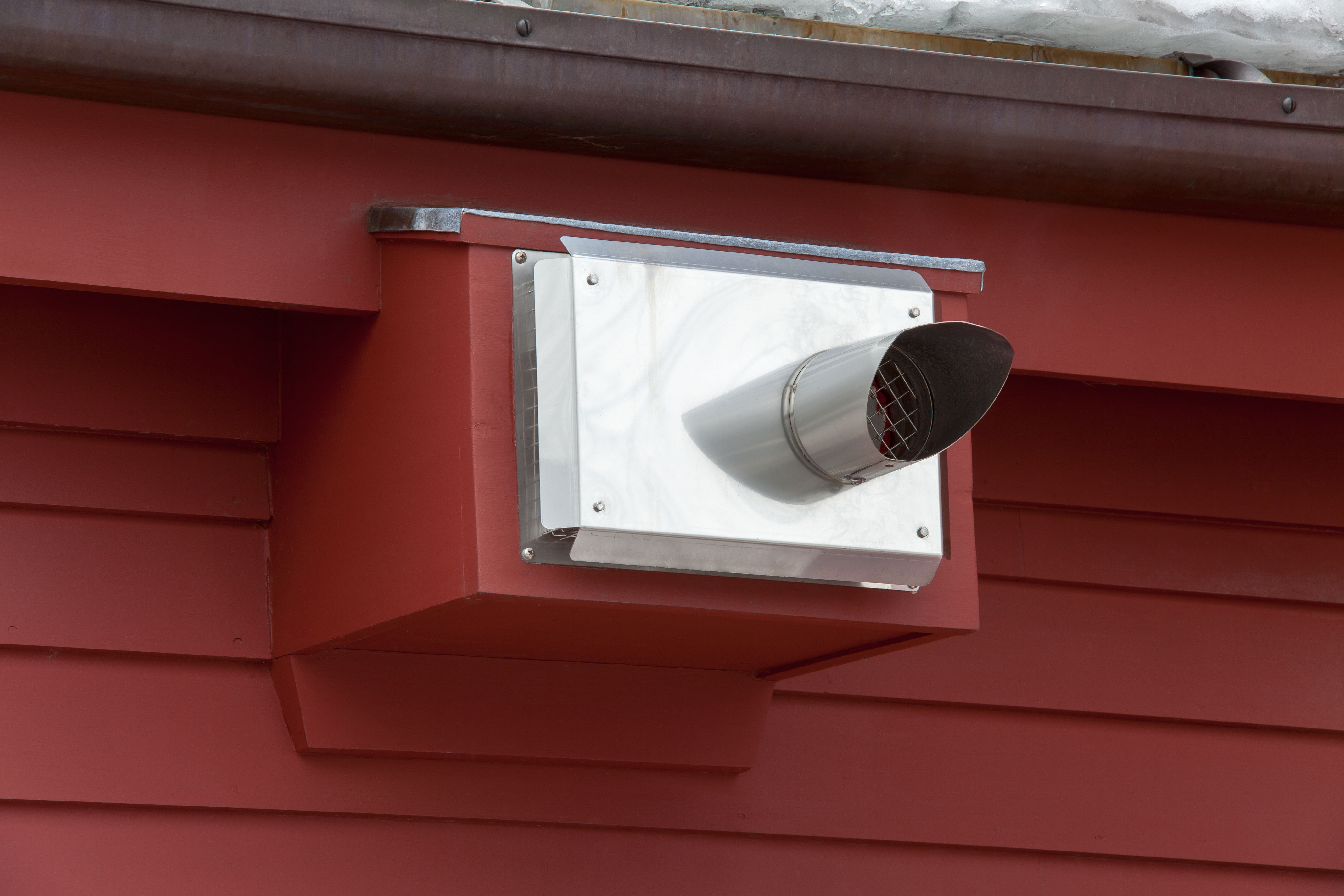 A boiler vent terminal with a stainless hood on a red clapboard wall